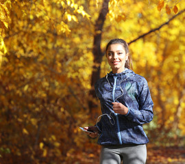 Young beautiful woman running in autumn park and listening to music with headphones.