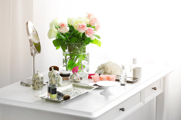 Bouquet of roses and cosmetic set on light dressing table