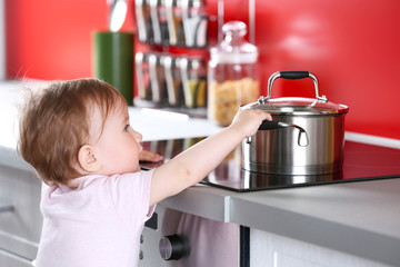 Little child playing with pan and electric stove in the kitchen