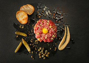 Steak tartar with bread and pickles on black background
