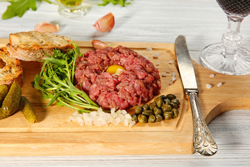 Steak tartar with chopped onion and herbs on wooden board