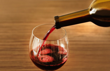 Red wine pouring in glass on wooden background