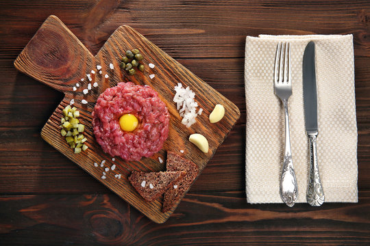 Steak tartar with chopped onion and pickles on wooden board