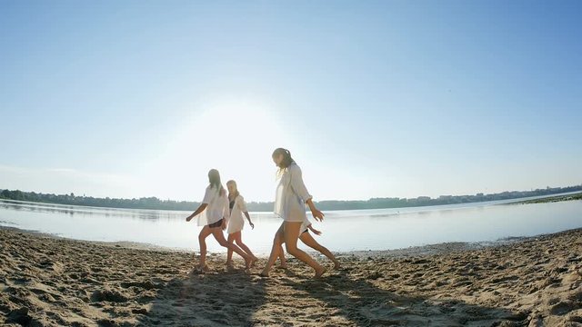 Dance performance of four girls on sand beach near lake at dawn