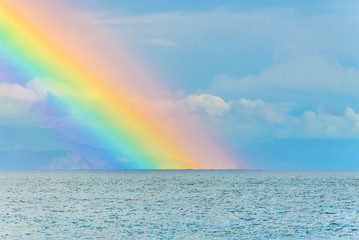 Beautiful seascape with big bright rainbow in clouds after the rain above the sea waves surface and mountains © EMrpize