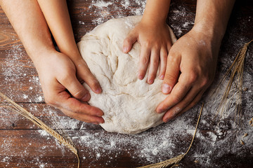 Father and child hands prepares the dough with flour, rolling pin and wheat ears on rustic wooden...
