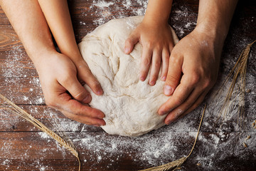 Father and child hands prepares the dough with flour, rolling pin and wheat ears on rustic wooden...
