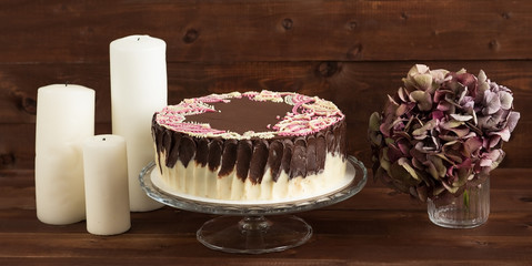 Cake on a Vintage stand, flowers, candles. Wooden background.