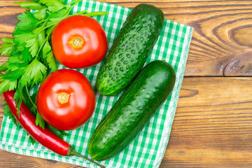 Backyard vegetables, tomatoes, cucumber, chilli pepper, parsley on napkin, wooden background.