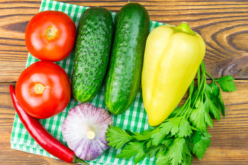 Backyard vegetables, tomatoes, cucumber, garlic, pepper, parsley on napkin, wooden background.