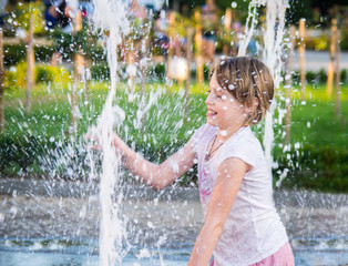 Happy girl having fun between water splashes in fountain . Sunny summer day in the city.