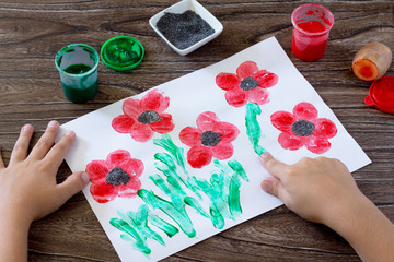 Drawing on paper poppies, child draws fingers grass. Glue, paint