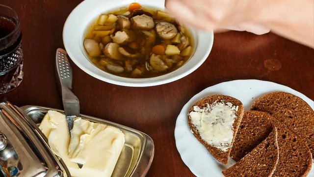 man eating soup with his left hand. left-handed. mushroom soup. bread. butter.