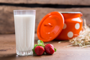 Glass of milk beside strawberries. Hay and milk can. Eat organic food. Care about your health.