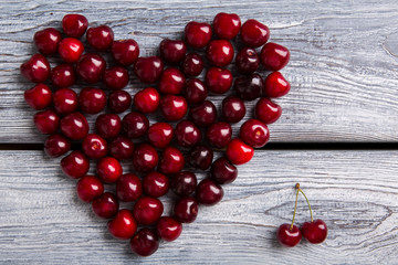 Heart made of dark cherries. Red fruit on wooden background. Summer sends love. Particles of art.