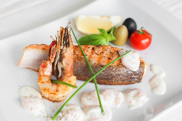 Grilled salmon and shrimp with cream sauce on white plate. Traditional mediterranean prepared seafood