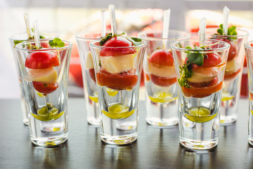 Catering for party. Close up of appetizers with cherry tomatoes, green olives, olive oil, cheese and spices in short glasses on wood brown table.