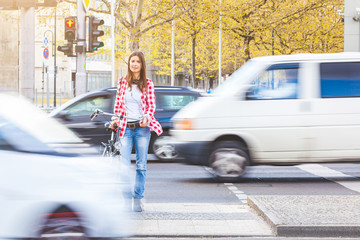 Young woman with bicycle waiting to cross the street at red signal in Berlin. There are blurred...