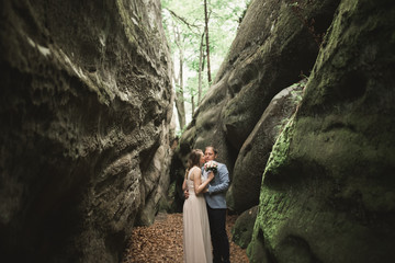 Gorgeous wedding couple kissing and hugging in forest with big rocks