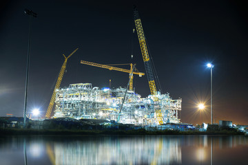 Construction of oil and gas refinery at night with water reflection