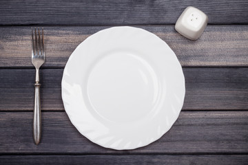 empty plate, fork and salt shaker on wooden table, top view