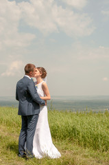 The groom kisses the bride on background of green grass outdoors