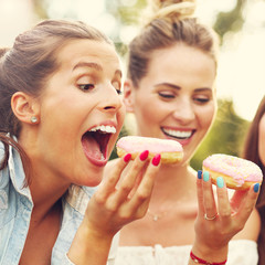 Happy group of friends eating donuts outdoors