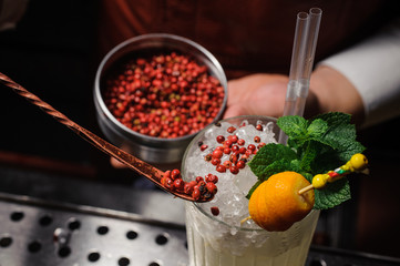 Barman is decorating cocktail with pink pepper