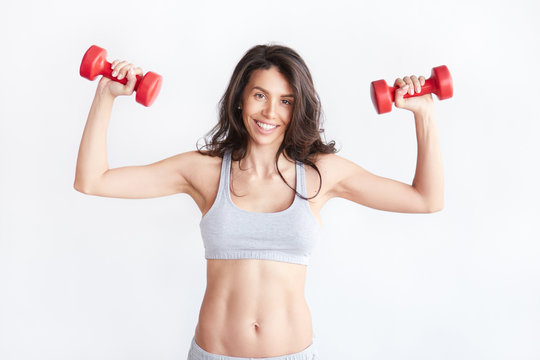 Smiling athletic woman pumping up muscles with dumbbells
