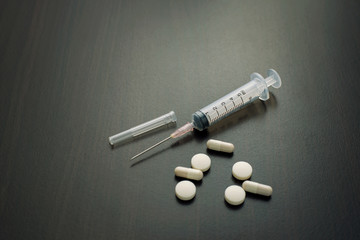 Syringe and pills on a wooden table