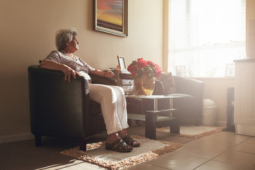 Senior woman sitting alone on a chair at home - Powered by Adobe
