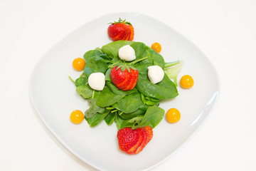Salad with fresh spinach, strawberries, mozzarella and physalis on a white plate