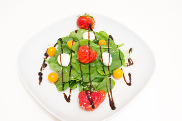 Salad with fresh spinach, strawberries, mozzarella and physalis on a white plate