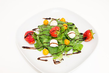 Salad with fresh spinach, strawberries, mozzarella and physalis on a white plate