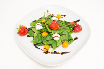 Salad with fresh spinach, strawberries, mozzarella and physalis on a white plate