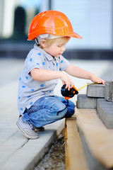 Little builder in hardhats with ruler working outdoors