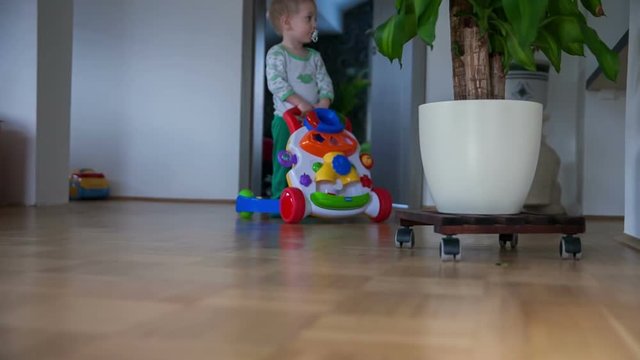 A Small Boy Is Pushing A Little Trolley And Playing In The Living Room. He's Also Having A Pacifier In His Mouth. Close-up Shot.
