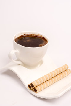 White cup of coffee with wafer chocolate cream rolls