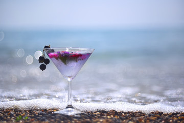 glass with a cooling summer drink in the magical light, sparkling drops of water on the beach. blurred gentle cheerful image with magic bokeh. Natural joyful sunny summer background.
