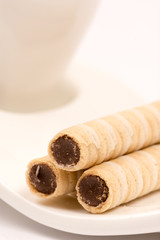 Wafer chocolate cream rolls on the plate of coffee