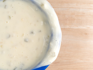 Messy bowl of tartar sauce on a wood table top close view.