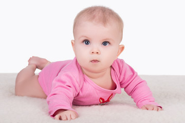 cute little baby girl with big blue eyes in pink bodysuit lying on a blanket and try crawling