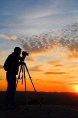 Silhouette of a nature photographer framing a shot, taking pictures at sunset in the mountains