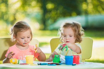 Two-year old girls painting with poster paintings together against green lawn