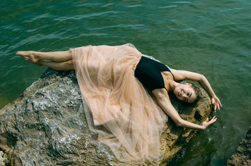 gymnast girl in a dress lying on the rocks, depicts flying ballerina dancing
