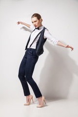 fashion model in black trousers, top, bow tie and vest posing over white