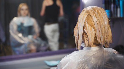 Professional hair coloring beauty studio. The girl in the client chair looking at reflection in the mirror.