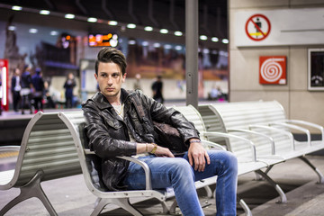 Young man traveling, sitting next to train timetable in railway station