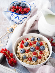 Oatmeal porridge with blueberries and red currants on rustic woo