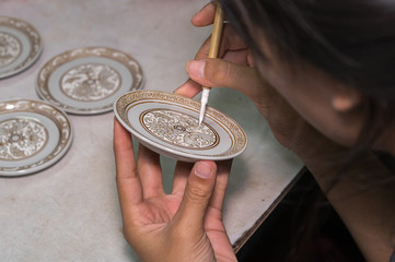 A pottery decorator finishing a ceramic small cup with floral motifs 
